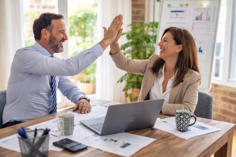 Een man en vrouw die een high-five aan elkaar geven tijdens het werken.